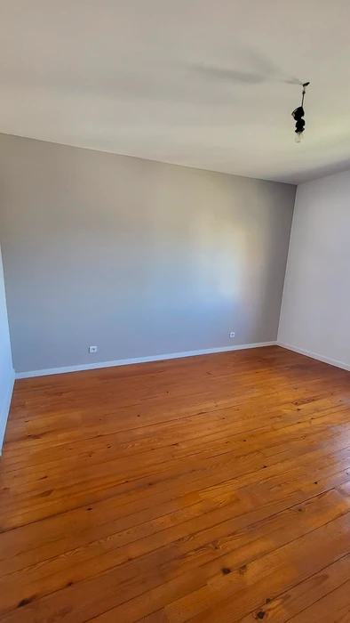 Pièce vide rénovée, murs peints en gris clair, parquet en bois massif teinte miel avec nœuds apparents, pose en lames larges parallèles