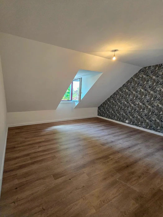 Pièce mansardée vide avec parquet stratifié chêne clair, murs blancs et plafond en pente