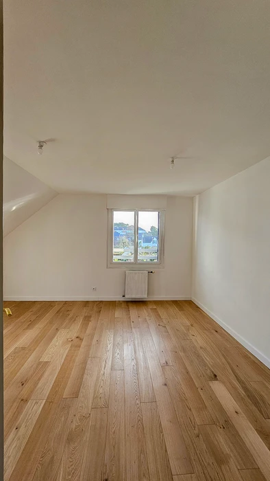 Pièce vide en combles aménagés, murs blancs, parquet massif chêne clair format bâtons rompus, plafond mansardé avec rampant