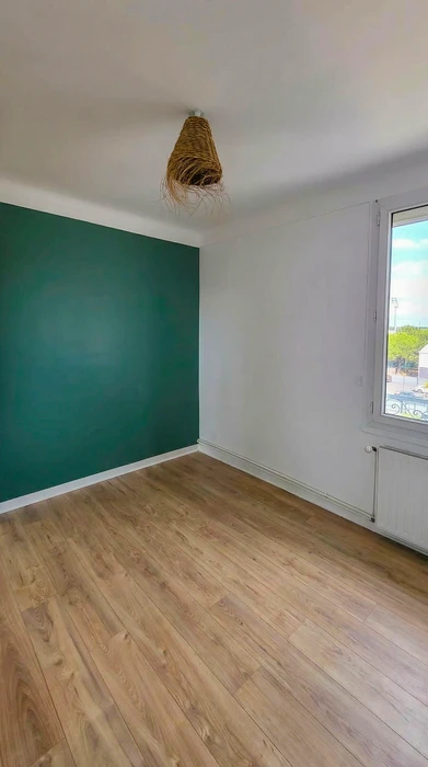 Pièce vide rénovée, mur d'accent vert émeraude, parquet stratifié chêne clair, murs blancs, fenêtre PVC blanc avec radiateur en fonte