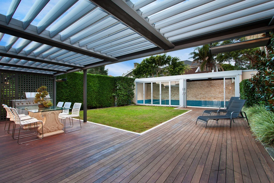 Terrasse extérieure moderne avec pergola à lames orientables, deck en bois exotique, salon de jardin design et piscine couverte vitrée