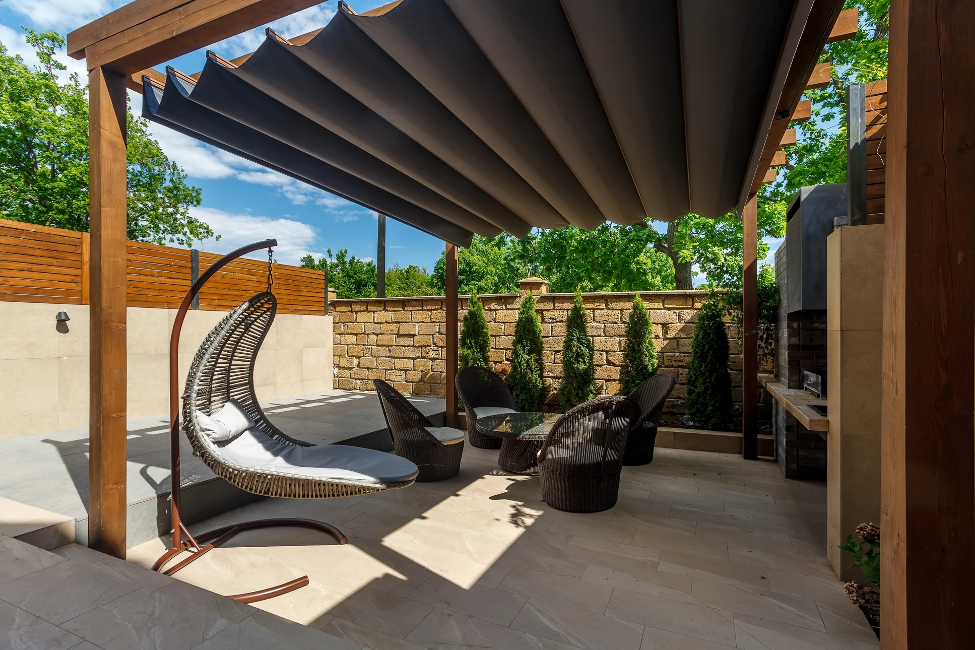 Homme se détendant sur une terrasse aménagée sous pergola en bois avec mobilier de jardin, fontaine décorative et végétation luxuriante